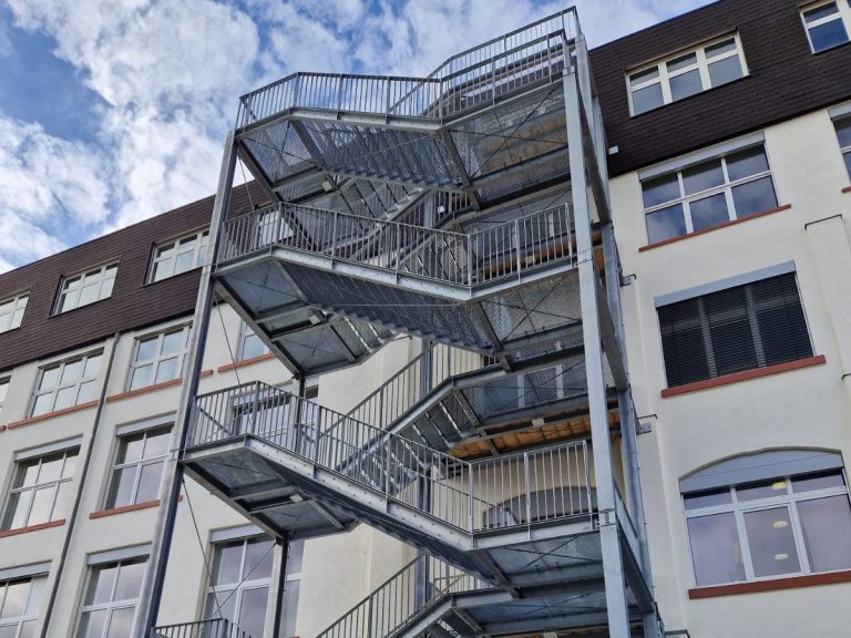 Metallene Feuertreppe an der Fassade eines mehrstöckigen Gebäudes.