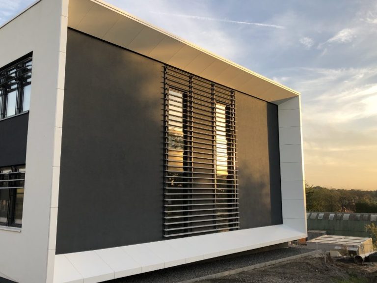 Moderne Architektur mit grauer Fassade und Sonnenschutzlamellen bei Sonnenuntergang.
